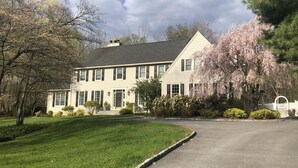 A two-story house with a front lawn, a driveway, and a white picket fence. - Country Living with Heated Pool and Hot Tub (Bedford)