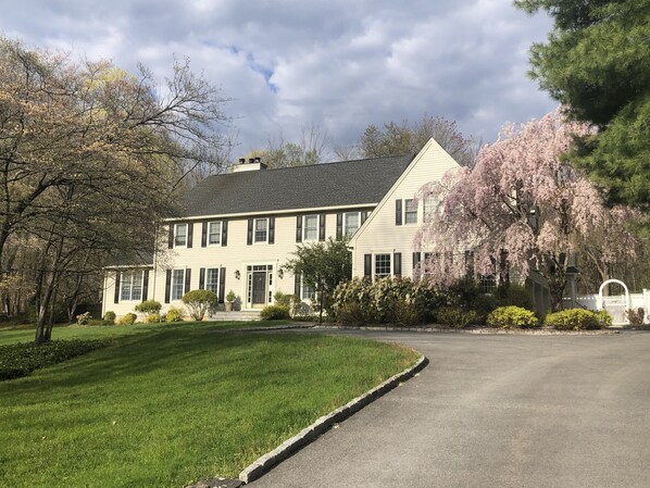 A two-story house with a front lawn, a driveway, and a white picket fence. - Country Living with Heated Pool and Hot Tub (Bedford)