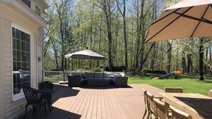 A wooden deck with outdoor furniture, including a sofa and chairs, and a large umbrella providing shade. - Country Living with Heated Pool and Hot Tub (Bedford)