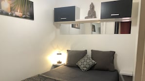 Ein Schlafzimmer mit einem Bett, Kissen, einem Nachttisch, einem an der Wand befestigten Regal mit einer Statue und einem Spiegel.