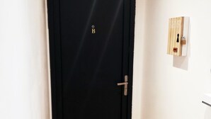 Eine schwarze Tür mit Griff und Schlüsselloch, ein Holzboden und eine weiße Wand mit Lichtschalter und einer kleinen Holzleiste.