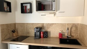 Eine kleine Küche mit integriertem Mikrowellenherd, Kaffeemaschine und Spüle.