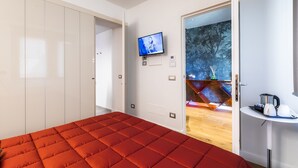 Ein modernes Hotelzimmer mit einem roten Bett, einem an der Wand befestigten Fernseher und Blick auf einen Wald durch eine Glastür.
