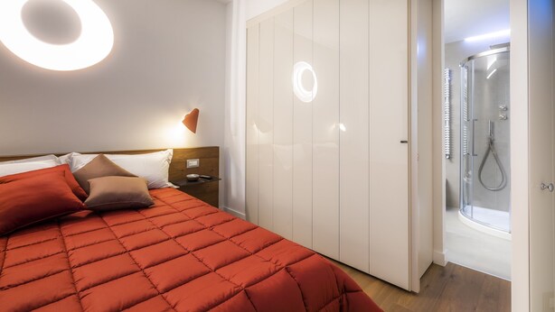 Ein Schlafzimmer mit Bett, Kissen, Nachttisch, Kleiderschrank und einer Duschkabine.