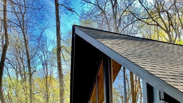 Una cabaña moderna con amplios ventanales, una terraza de madera y vistas a zona boscosa.