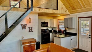 Amplio espacio tipo loft con una escalera de madera, cocina con muebles blancos y una zona de estar acogedora.