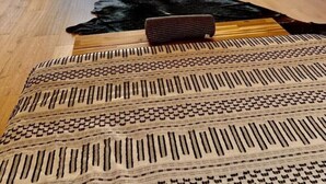 Una habitación con techo inclinado, suelo de madera, alfombra de piel sintética negra y alfombra estampada.