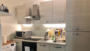 A compact kitchen with a washing machine, microwave, sink, and stainless steel cabinets.