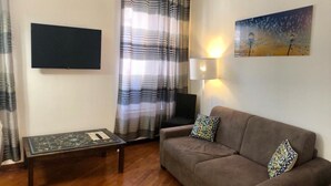 A living room with a sofa, a coffee table, a flat-screen TV, a lamp, and a painting on the wall.