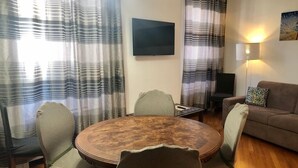A living room with a round wooden coffee table, two chairs, a sofa, and a TV mounted on the wall.