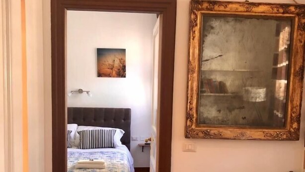 A bedroom with a bed, a nightstand, a framed picture, and a wooden floor.
