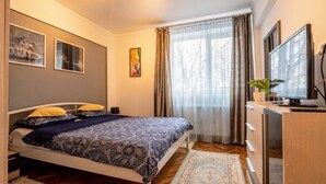 Un dormitorio con cama, un escritorio con computadora, televisor y ventana con cortinas.