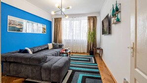Una sala de estar con un sofá modular, un ventanal con cortinas, una planta y un televisor montado en la pared.