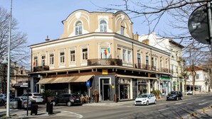 Un edificio en esquina con una cafetería en la planta baja, una farmacia y un restaurante.