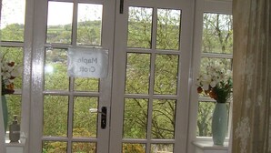 A room with a large glass door leading to a balcony. There is a sign on the door, a red bag on the floor, and a vase with flowers on the windowsill. - Cosy flat with a great view, near the centre of Hebden Bridge  (Hebden Bridge)