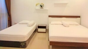 A hotel room with two beds, a nightstand, a small shelf with flowers, and a window with curtains. - Fams Homestay by FH Stay (Baturetno)