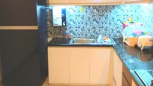 A compact kitchen with a black refrigerator, a tiled backsplash, and a small countertop with a sink. - Fams Homestay by FH Stay (Baturetno)