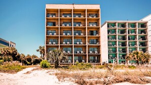 Un hotel de varios pisos con balcones, situado cerca de una zona de playa con arena.