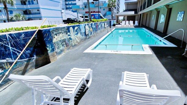 A rooftop pool area with two white lounge chairs, a blue and white mural, and a sign for Ocean Plaza. - South Seas Ocean Front (Myrtle Beach)