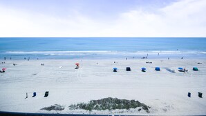 A beach with tents and umbrellas, a sandy shore, and the ocean in the background. - South Seas Ocean Front (Myrtle Beach)