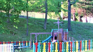 Un parque infantil con tobogán y columpios, rodeado por una valla de colores.