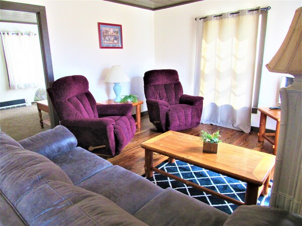 A living room with a sofa, two armchairs, a wooden coffee table, a lamp, and a picture frame on the wall.