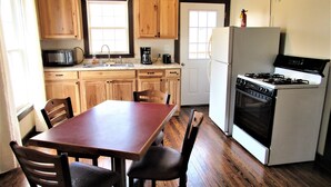 Una cocina con armarios de madera, estufa, refrigerador y una mesa de comedor con sillas.
