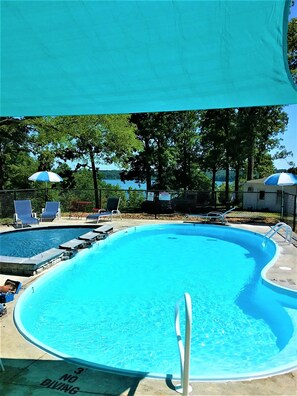 A swimming pool with lounge chairs and umbrellas, surrounded by trees and a view of the water.
