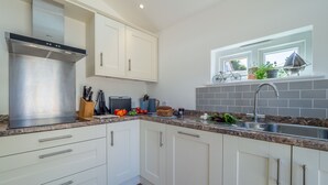 A modern kitchen with white cabinets, stainless steel appliances, and a window with a bicycle view. - Yew Tree Cottage is a modern eco-cottage (Westleton)