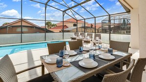 A glass-enclosed dining area with a pool view, wicker furniture, and a clear sky. - SO136CA - Amazing 4 Bedrooms Pool Home with Clubhouse Access (Davenport)