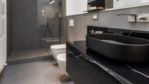 Un baño moderno con ducha envuelta en vidrio, lavabo de mármol negro y un espejo grande.