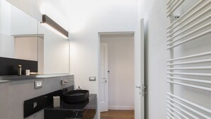 Un baño moderno con un lavamanos negro, paredes blancas y suelo de madera.