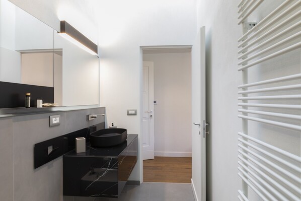 Un baño moderno con un lavamanos negro, paredes blancas y suelo de madera.