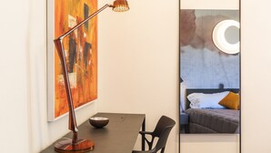 Habitación moderna con escritorio, silla y un gran espejo que refleja una cama con lámpara circular.