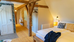 Une chambre avec un plafond en bois, un lit agrémenté d’oreillers à motifs, une table de chevet avec un livre et une tasse, et un porte-manteau suspendu.