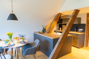 A modern kitchen with a wooden staircase, a dining area with a table set for breakfast, and a hanging pendant light. - Wohlfühlen mit Weitblick (Neusalza-Spremberg)