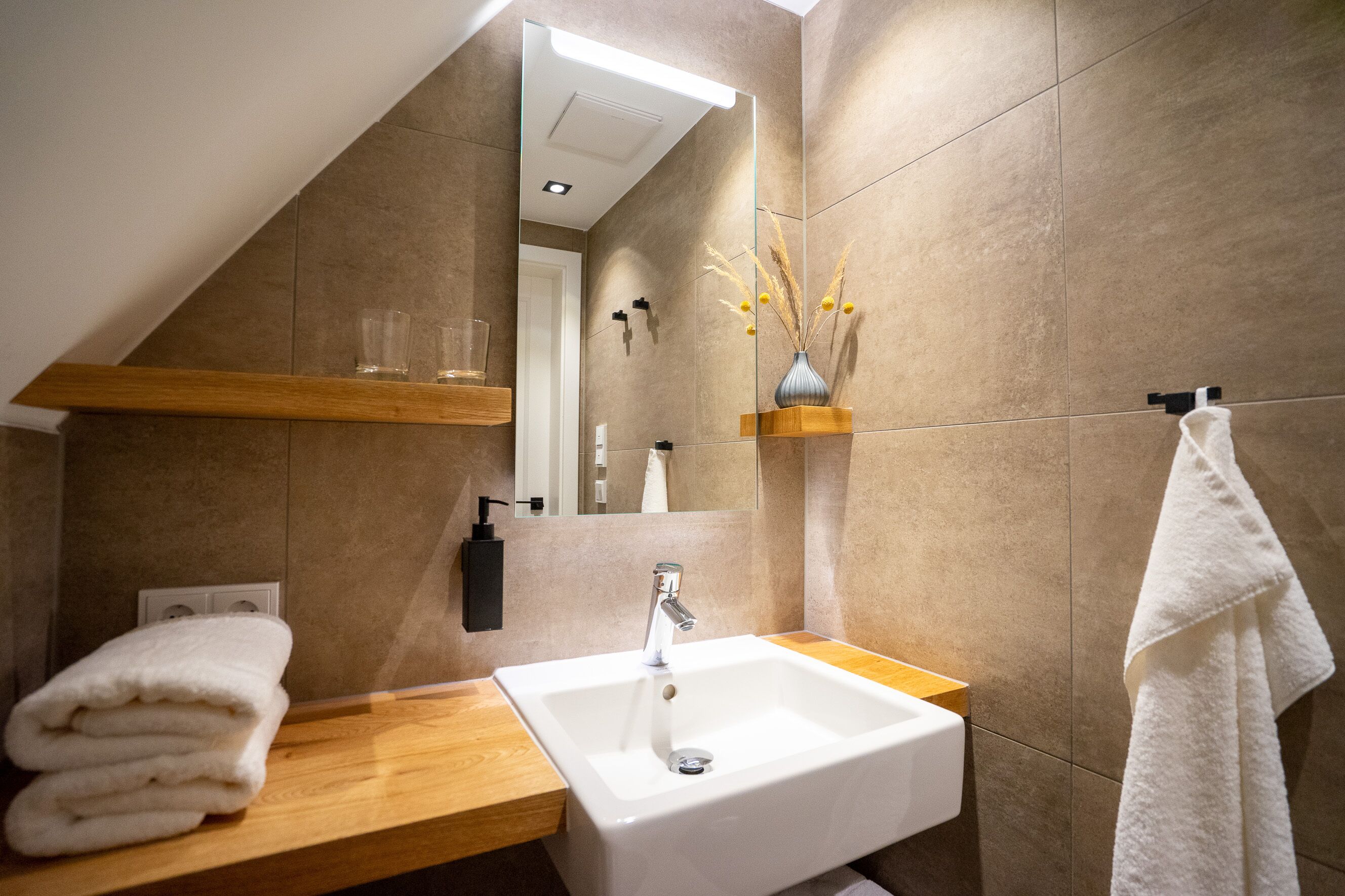 Un baño moderno con un lavamanos blanco, encimera de madera y un perchero para toallas.