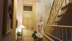 A staircase with ornate metal railings, a checkered floor, a chandelier, and a door with a painting on the wall. - Chateau Leconte, Beautiful Vintage House in Thessaloniki (Thessaloniki)