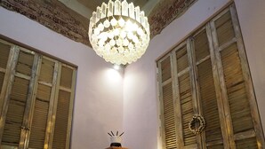 A dining area with a glass table, metal chairs, a chandelier, and a view of the outside through wooden shutters. - Chateau Leconte, Beautiful Vintage House in Thessaloniki (Thessaloniki)