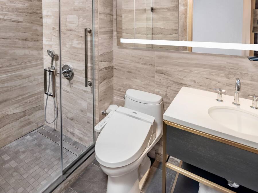 Ein modernes Badezimmer mit einer gläsernen Duschkabine, einer weißen Toilette und einem Waschtisch mit Spiegel.