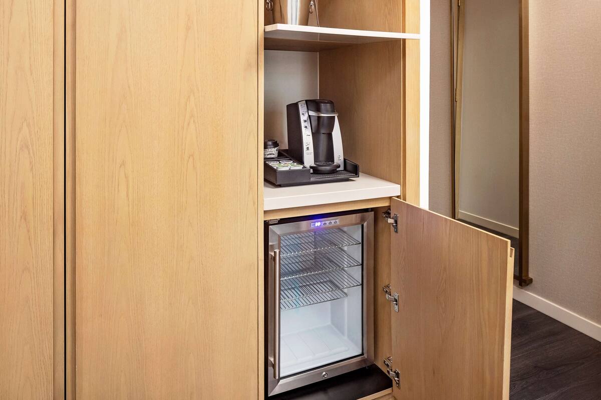 A compact refrigerator with a coffee maker on top, built into a wooden cabinet.
