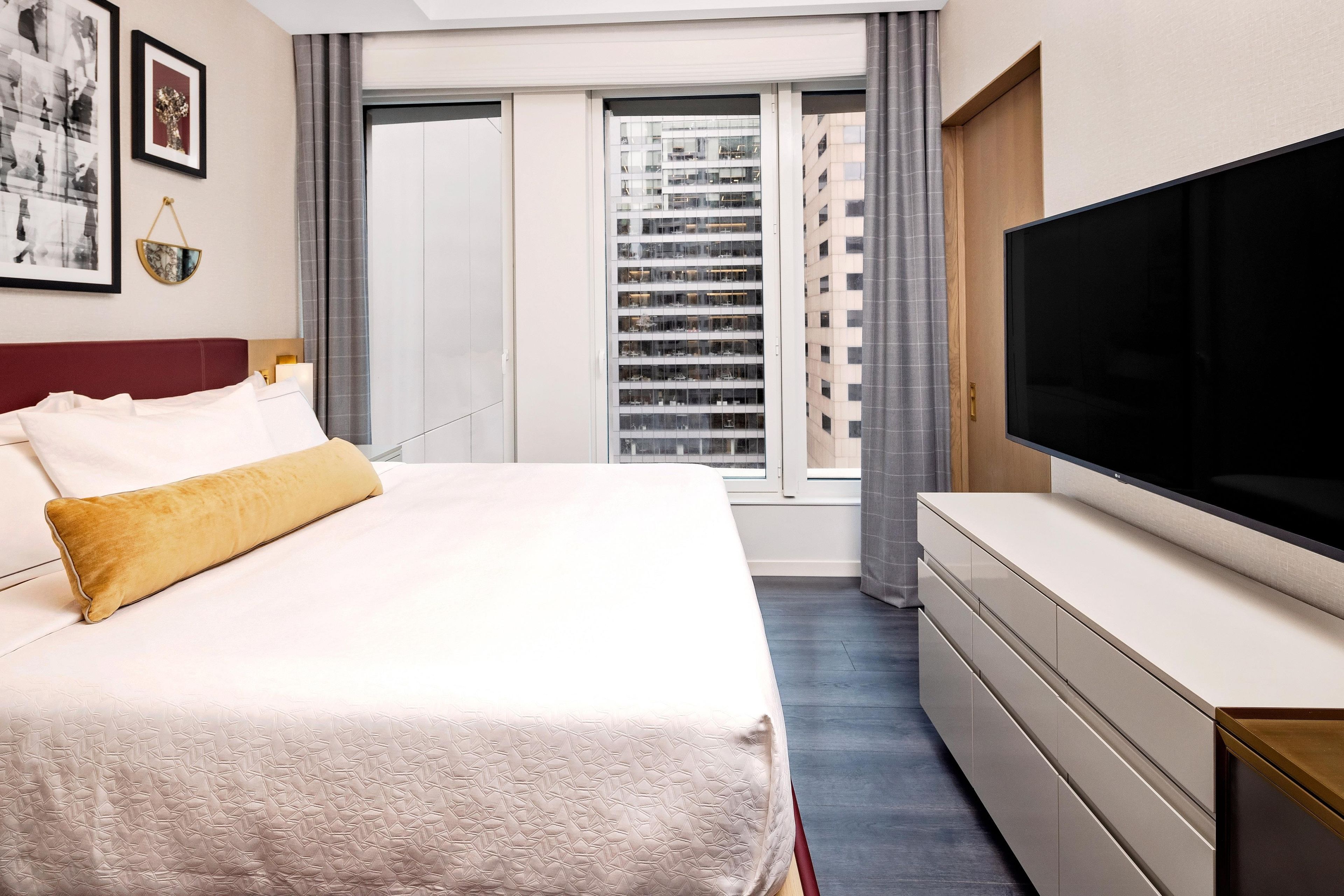 Habitación de hotel con cama, televisor de pantalla plana, cómoda y ventana con vista a la ciudad.