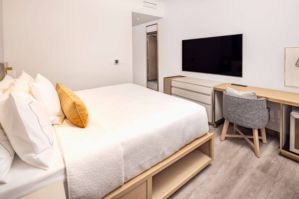 A modern hotel room with a bed, a desk, a chair, and a TV.