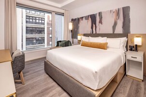Une chambre d’hôtel avec un grand lit, un bureau, une chaise et une vue sur la ville par la fenêtre.
