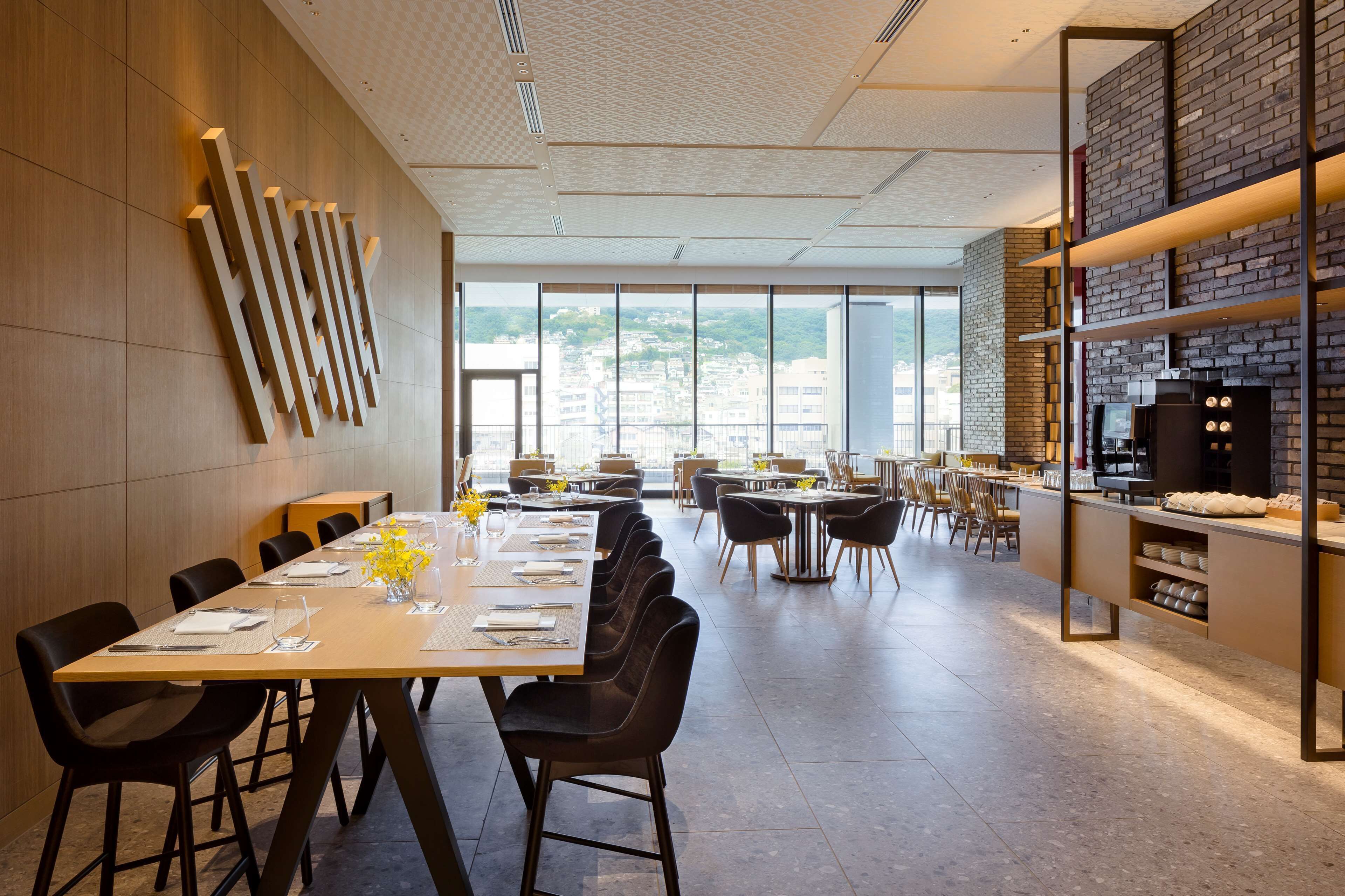 A modern dining area with a long table, black chairs, and a brick wall with shelves.