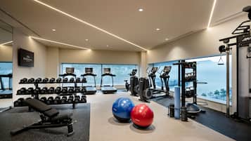 A modern gym with exercise equipment, a bench, dumbbells, and a view of the city.