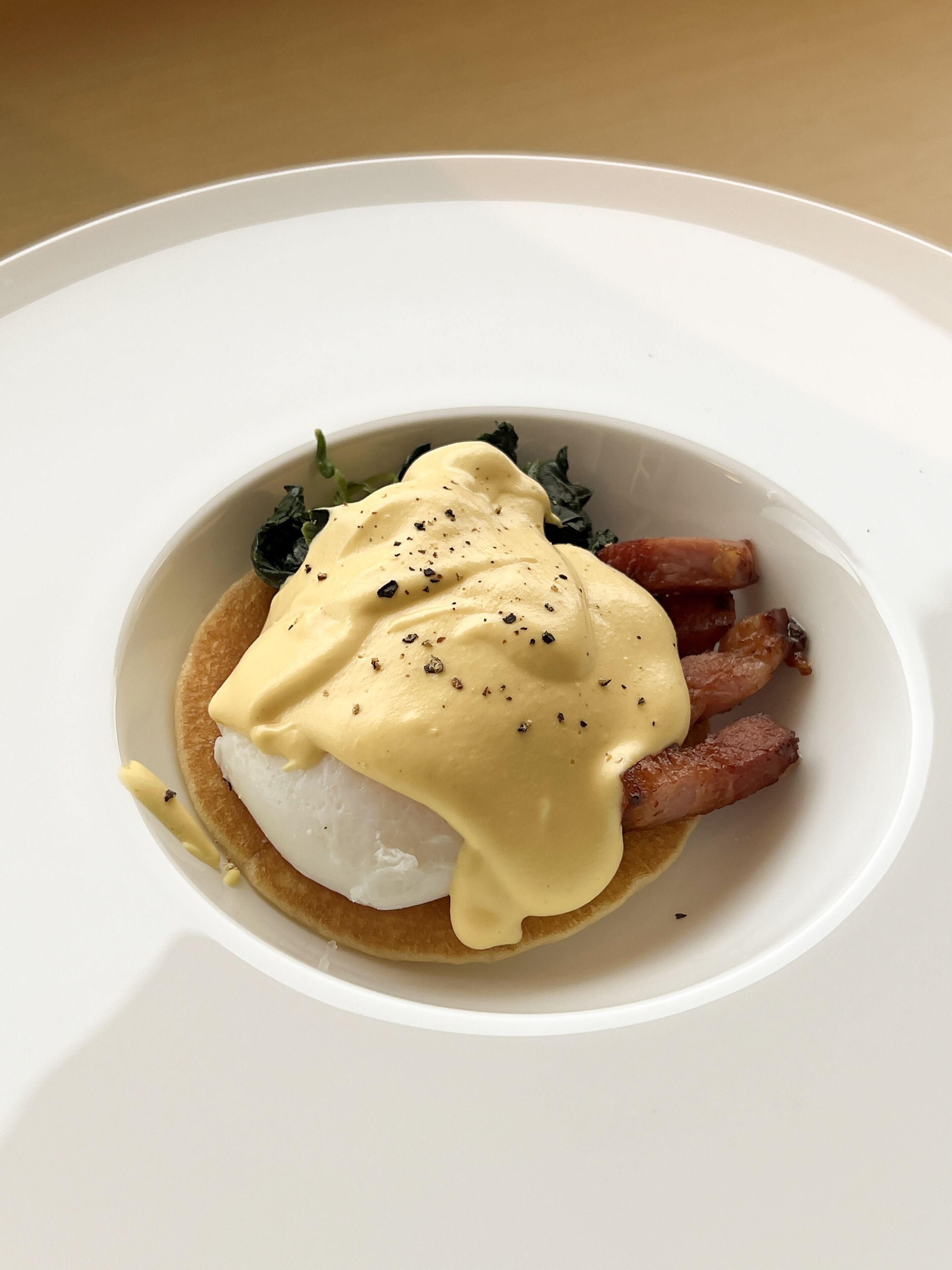 Une assiette blanche avec un œuf poché, de la sauce hollandaise et du bacon.
