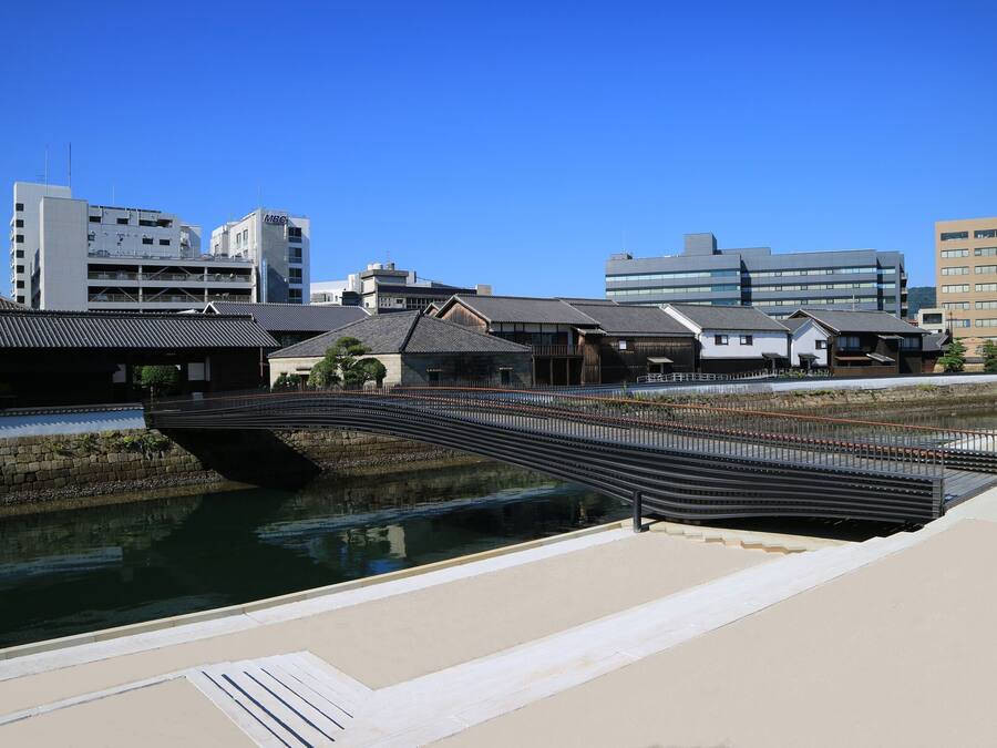 Un puente moderno sobre un canal, con edificios tradicionales al fondo.