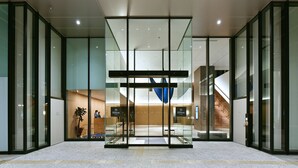 Una entrada de hotel moderna con puertas de cristal, un mostrador de recepción y una escalera que conduce a los pisos superiores.