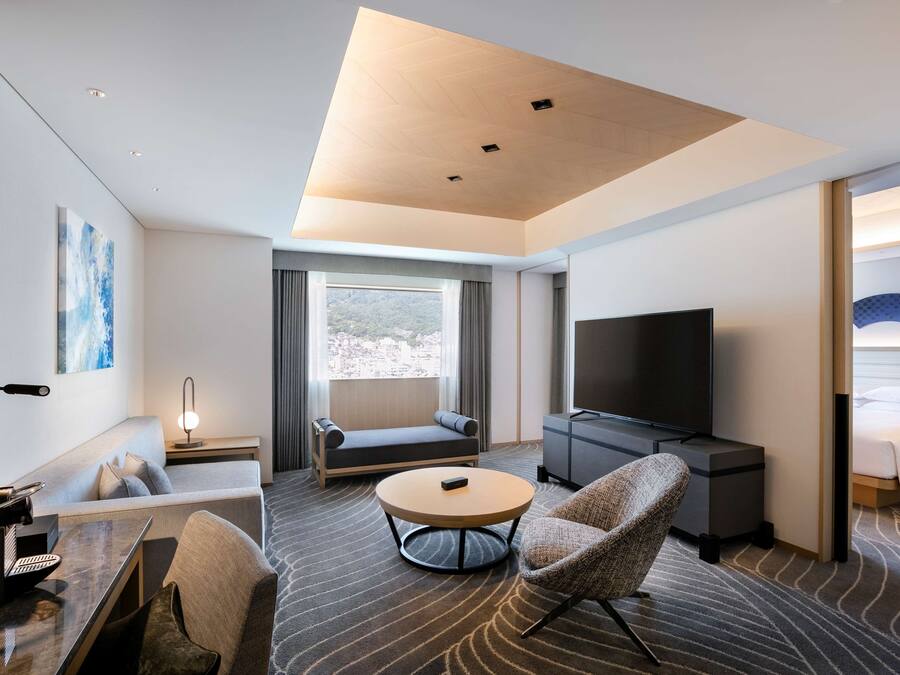 Une chambre d’hôtel moderne équipée d’un canapé, d’une table basse ronde, d’un téléviseur, d’un bureau avec une lampe et d’un lit.